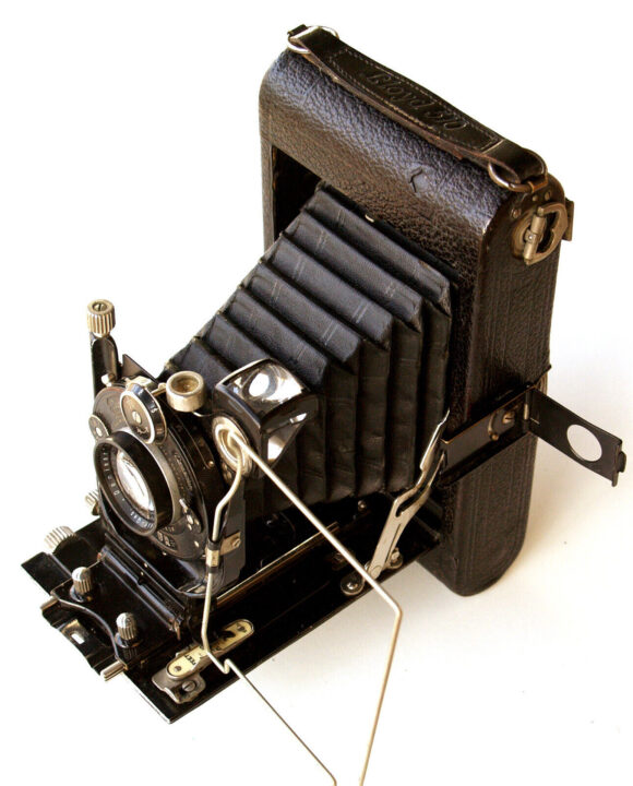 A vintage ICA Lloyd 510 folding camera with a black leather exterior and a bellows mechanism. The camera features a manual shutter and intricate metal detailing, showcasing a classic design from early photography.
