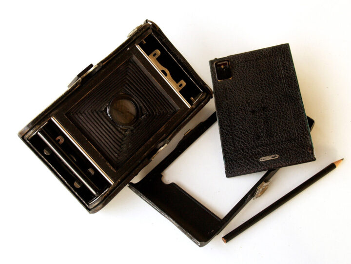 A vintage ICA Lloyd 510 camera with a black leather case, positioned alongside a pencil. The camera's lens is visible, and its inner workings are exposed, highlighting the classic design and craftsmanship.