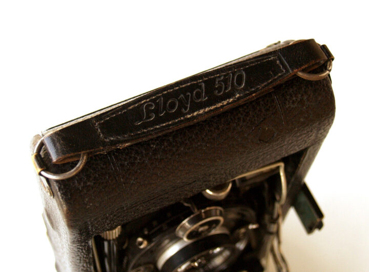 An antique camera with a black leather case, featuring the engraved name "Lloyd 510" on the strap, presented from a top-down view.