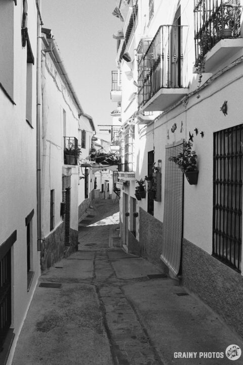 A black-and-white photo of a pretty narrow street in Jubrique with townhouses on both sides.