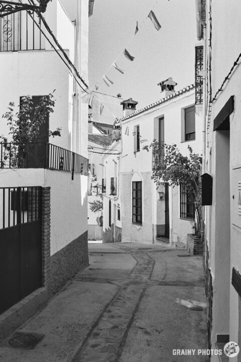 A black-and-white photo of a pretty narrow street in Jubrique with townhouses on both sides.