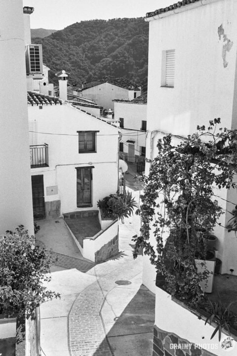 A black-and-white photo looking down on a narrow meandering cobbled street amongst white houses.