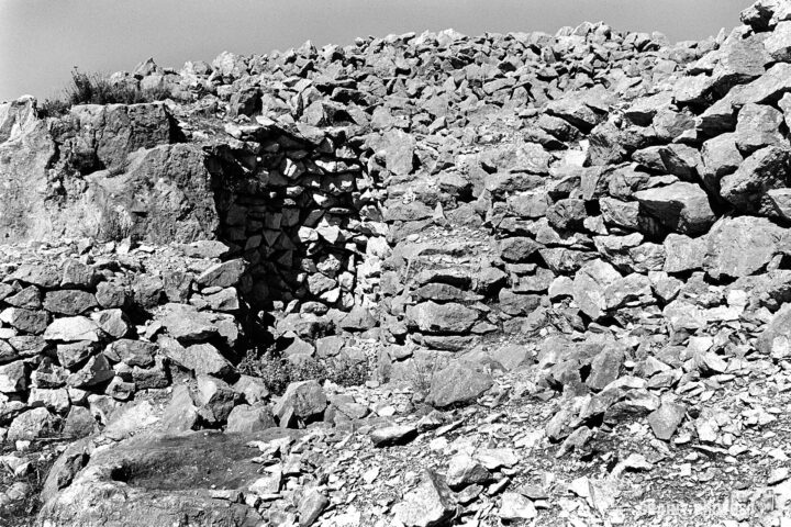 Black and white photograph of a weathered rocks and the remnants of an ancient stone mason’s hut, in a rugged terrain.