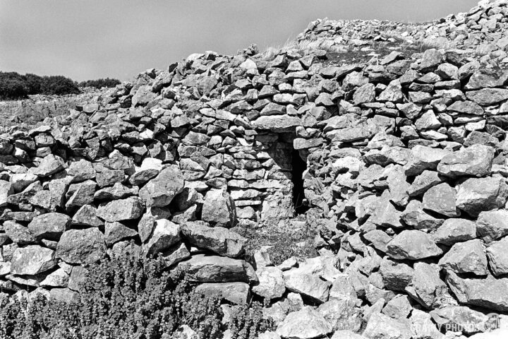 The ruins of a stone structure at Los Caracoles with a partially collapsed entrance to a stone mason’s hut. The scene is in black and white, highlighting the texture of the rocks and the rustic setting.
