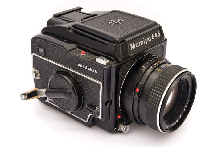 A Mamiya 645 medium-format film camera, featuring a black body, a prominent lens, and various dials and controls for photography. It is designed for capturing high-quality images.