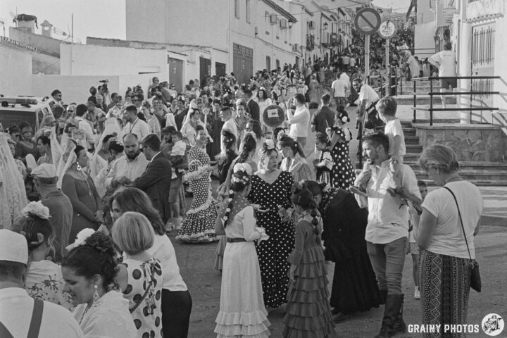 A bustling street scene filled with people celebrating, dressed in traditional attire, including polka dot  and Flamenco dresses. The crowd is lively, with families and friends enjoying the festivities in a vibrant, festive atmosphere.
